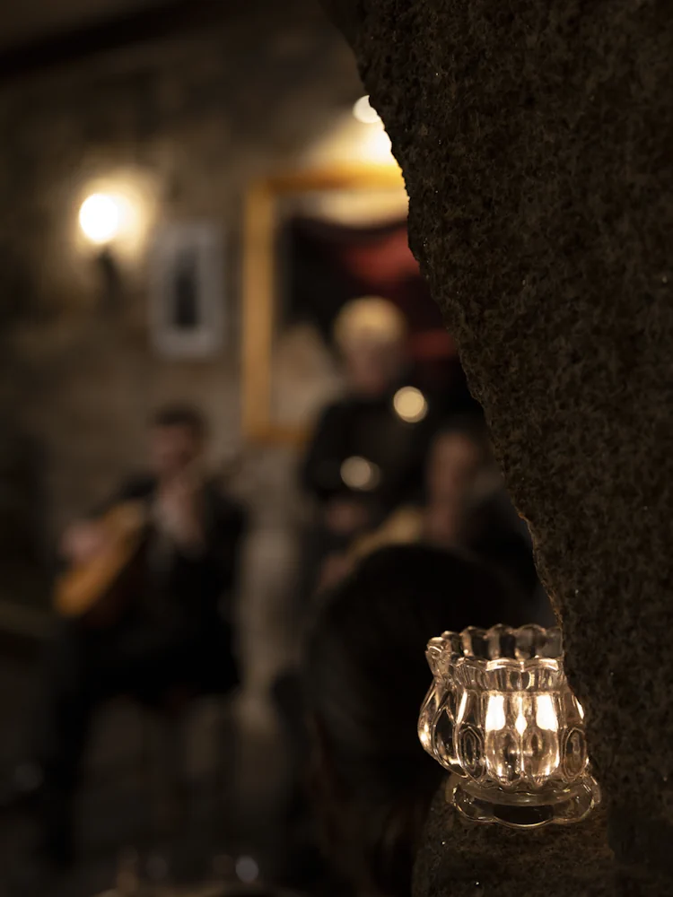 Vela em copo de vidro sobre coluna de granito, com músicos de Fado desfocados em fundo num concerto ao vivo no Porto, no Fado Maior do Porto