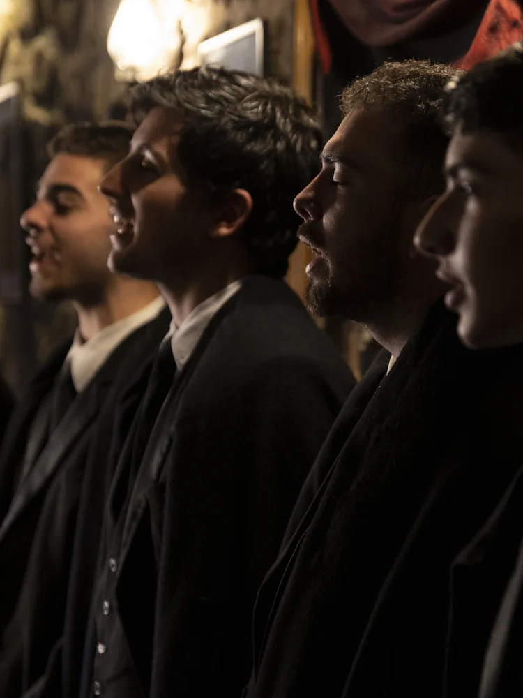 Quatro fadistas de Fado de Coimbra de capas negras a cantar em perfil num concerto de Fado ao vivo no Porto, no Fado Maior do Porto